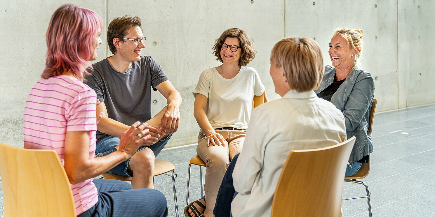 Studierende sitzen in einem Stuhlkreis und unterhalten sich. 