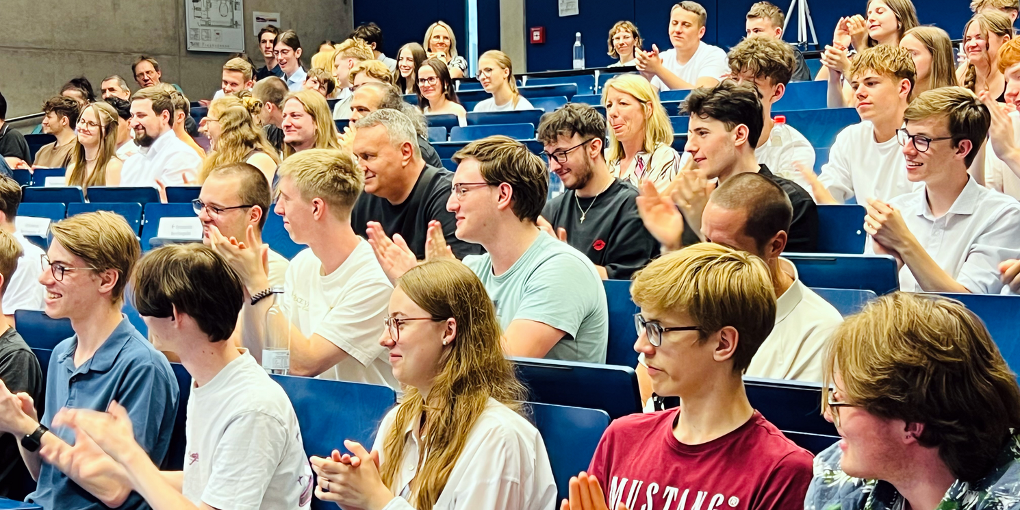 Ein voller Hörsaal, die Schüler klatschen und nehmen ausgelassen an der Feier teil. 