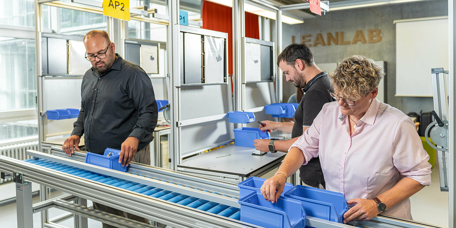 Drei Studierende arbeiten im LeanLab an einer Fertigungsstrecke. 