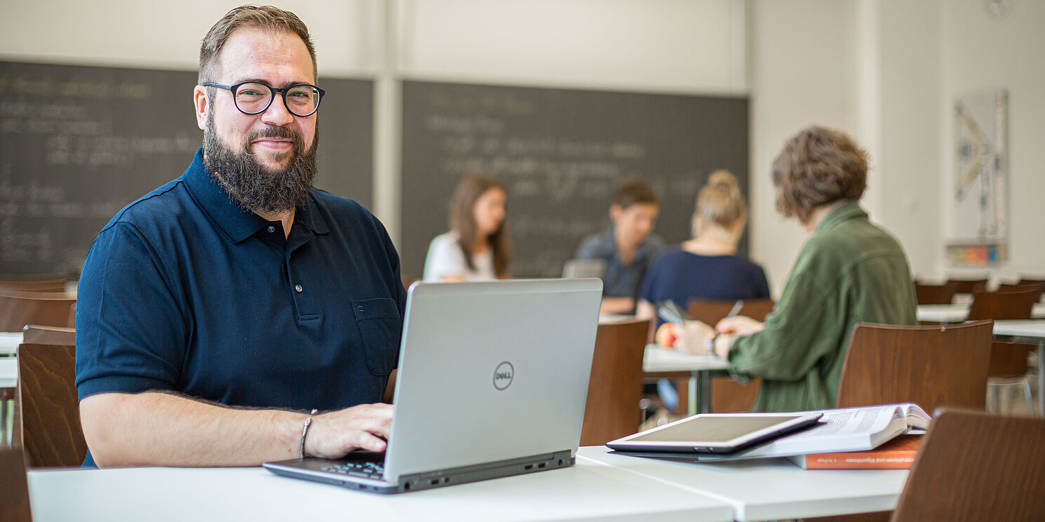 Ein Mann mittleren Alters sitzt an seinem Laptop in einem Seminarraum.