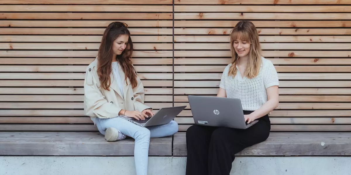 Zwei Studierende sitzen zusammen mit ihren Laptops