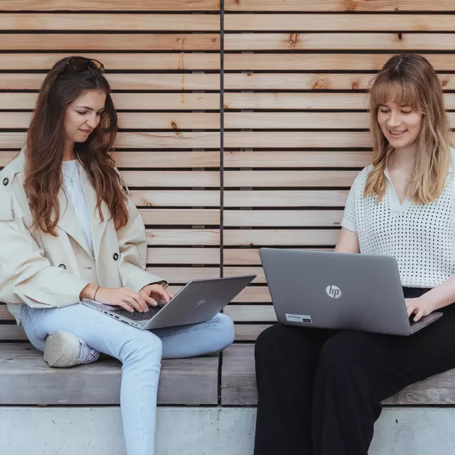 Zwei Studierende sitzen zusammen mit ihren Laptops