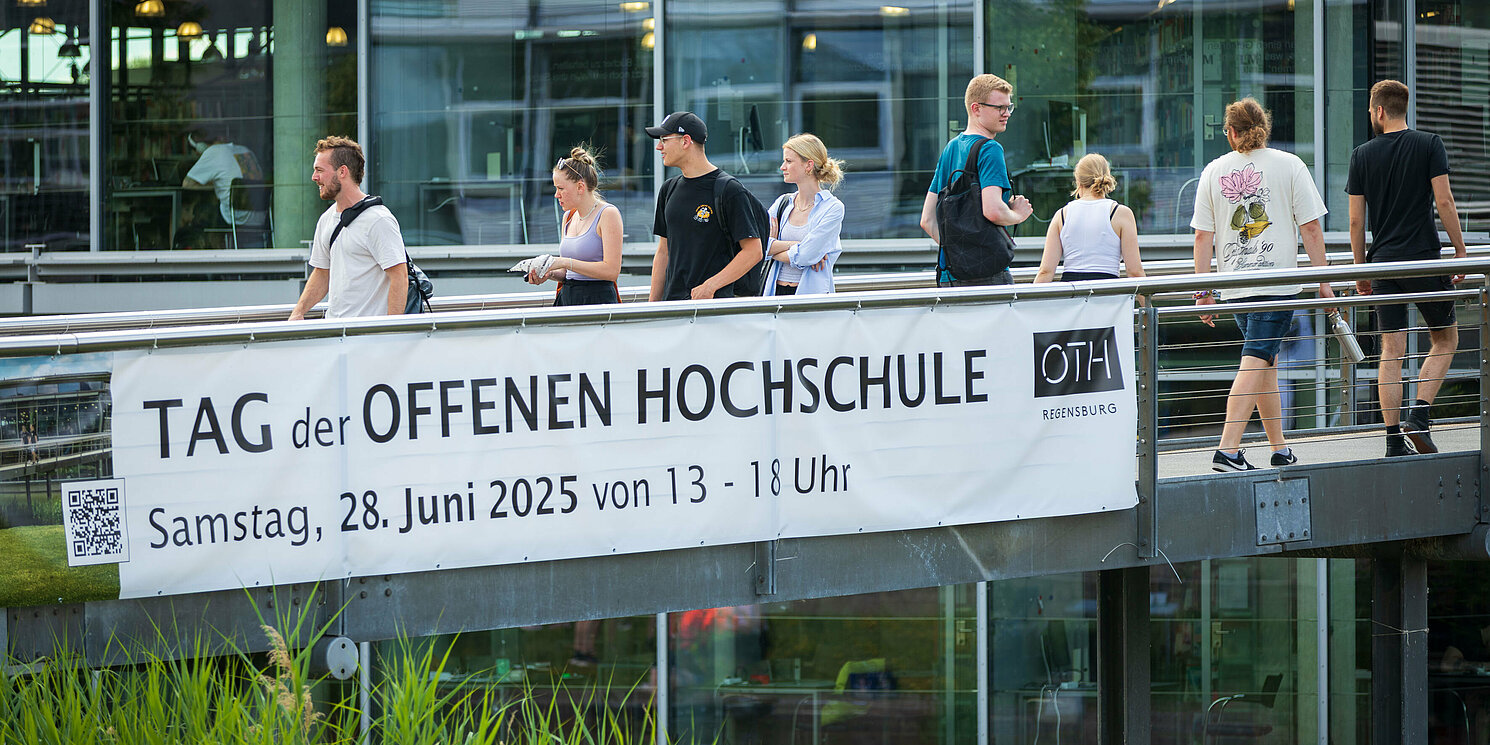 Personen laufen über Campus Brücke mit Banner zum Tag der offenen Hochschule der OTH Regensburg