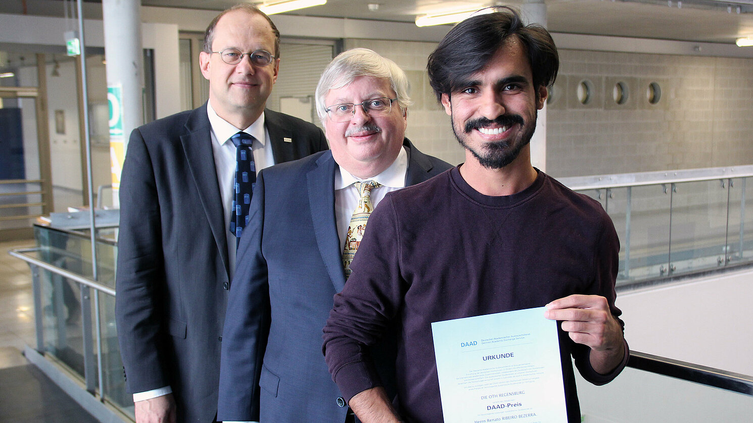 Den DAAD-Preis 2018 der OTH Regensburg hat Renato Ribeiro (rechts), Masterstudent der Historischen Bauforschung, erhalten. Vizepräsident Prof. Dr. Thomas Fuhrmann (links) und der Leiter des Akademischen Auslandsamts Dr. Wilhelm Bomke haben ihm den Preis überreicht. Foto: Diana Feuerer, OTH Regensburg
