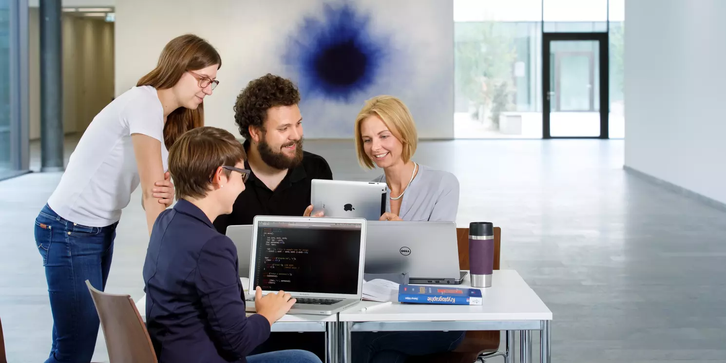 Hochschulzertifikat Technology Skills for Business Professionals berufsbegleitend absolvieren Vier Studierende sind in einer Lerngruppe mit Laptops und Büchern zusammen gekommen