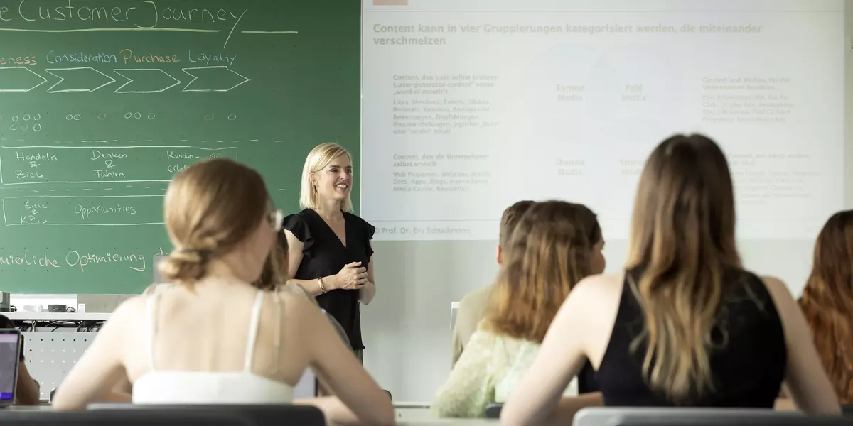 Studierende sitzen in der Vorlesung bei Prof. Dr. Schuckmann. Links im Bild ist eine grüne Tafel.