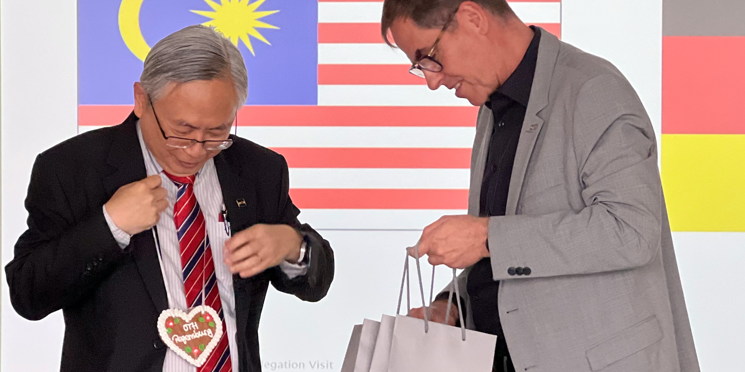 OTH-Präsident Prof. Dr. Ralph Schneider übergibt UTAR-Präsident Ir. Professor Dato' Dr. Ewe Hong Tat ein Lebkuchenherz mit der Aufschrift "OTH Regensburg" wie man es von einem Volksfest kennt.