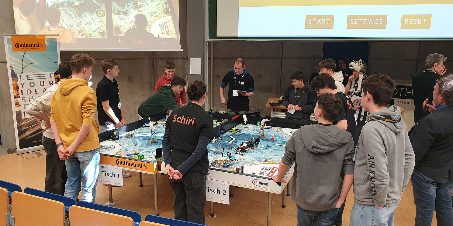 Mehrere Personen stehen um einen Tisch mit einer Lego-Versuchsstrecke.