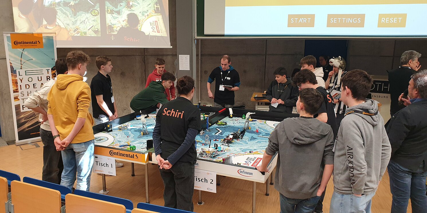 Mehrere Personen stehen um einen Tisch mit einer Lego-Versuchsstrecke.