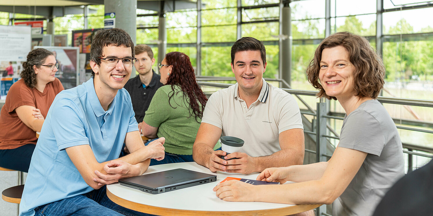 Studierende sitzen an einem Tisch in der Cafeteria und unterhalten sich.