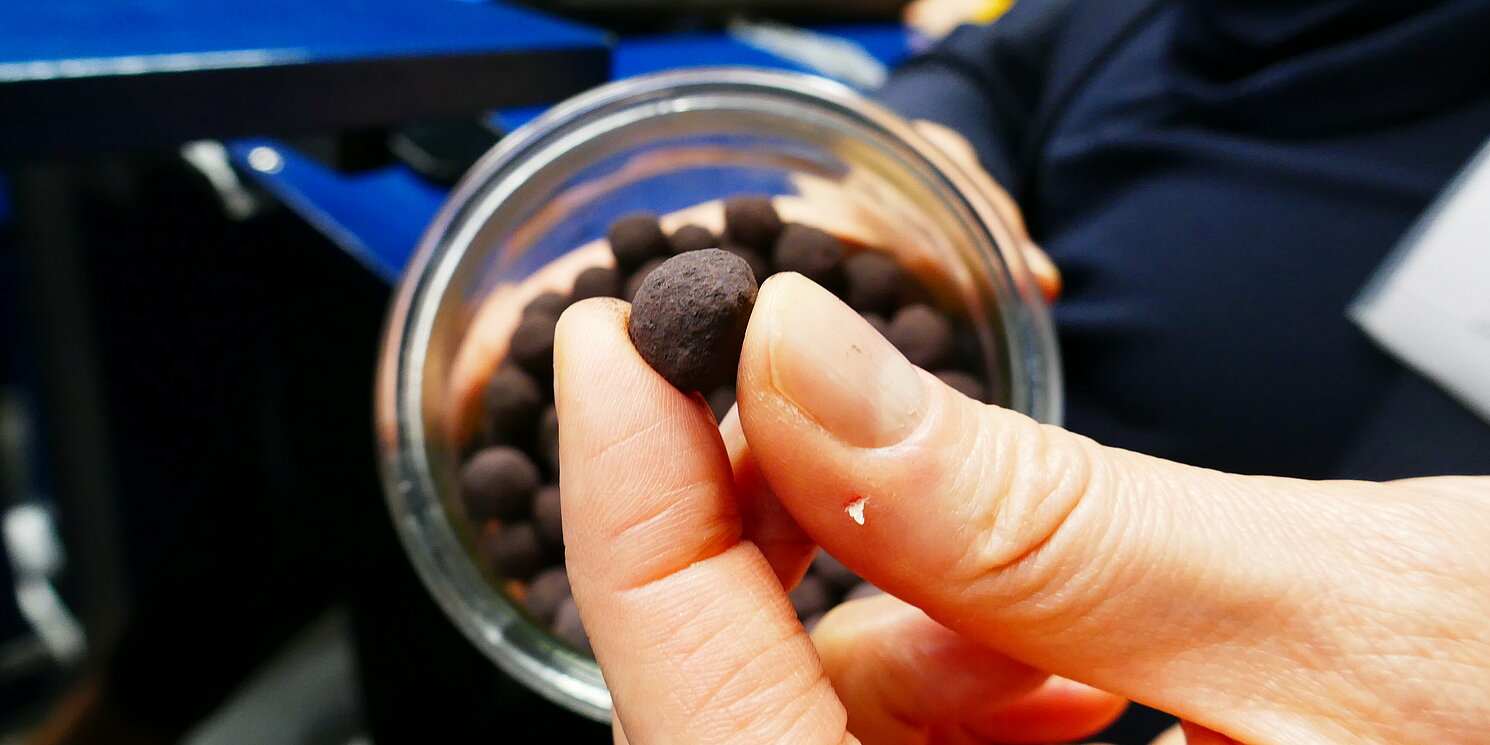 Eine Hand hält zwischen Daumen und Zeigefinger ein Eisenoxid-Pellet.