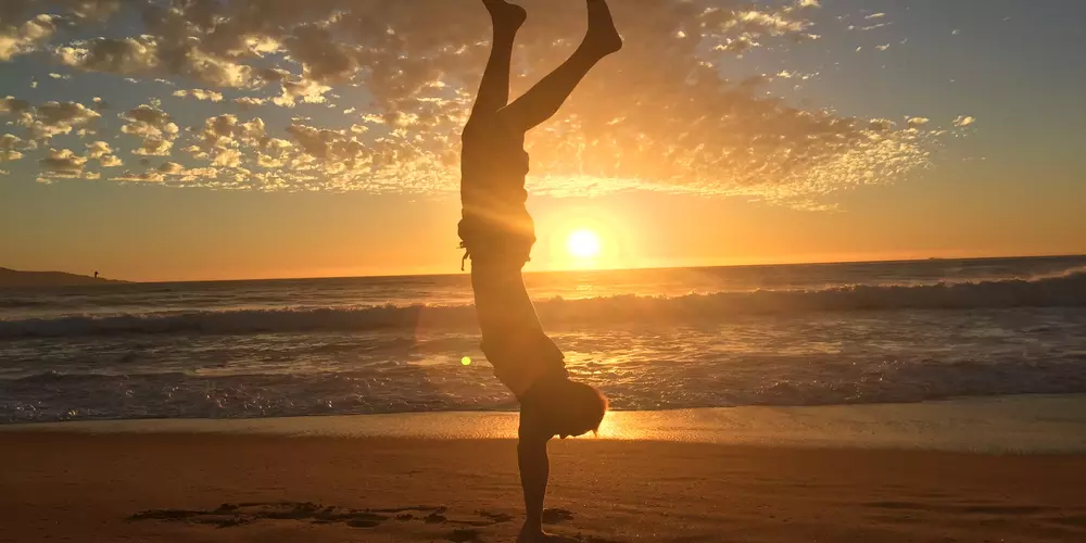 Student im Handstand am Strand bei Sonnenuntergang