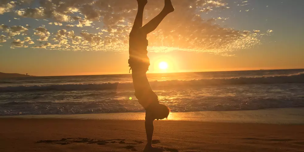 Student im Handstand am Strand bei Sonnenuntergang