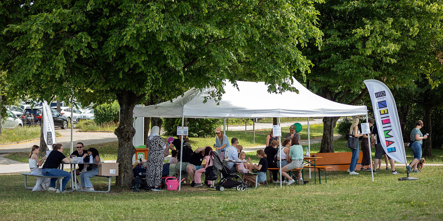Personen sitzen auf Campuswiese bei der Station für Kinder beim Tag der offenen Hochschule der OTH Regensburg