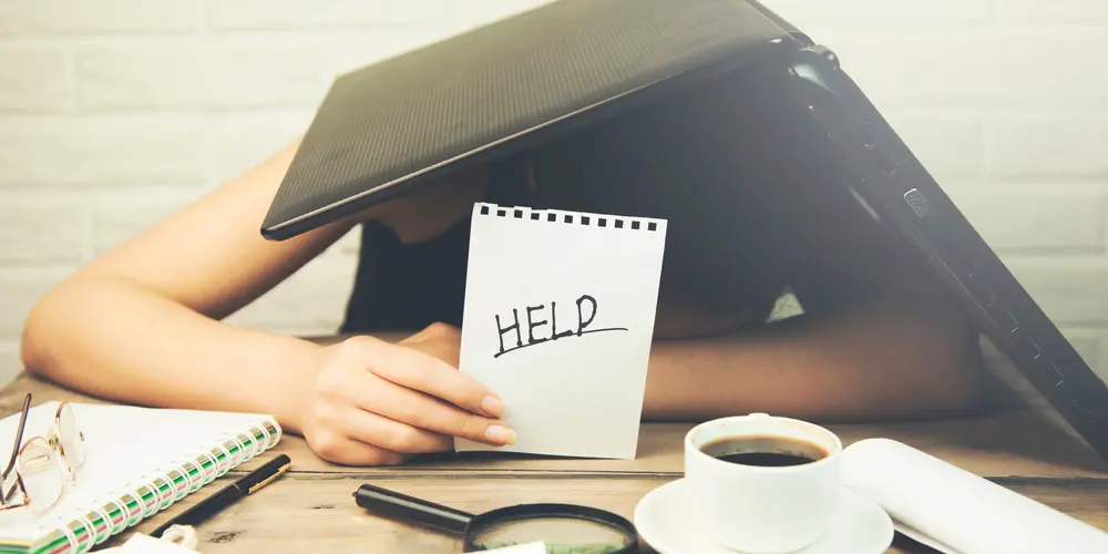 Mensch unter Laptop mit Hilfe-Schild in der Hand