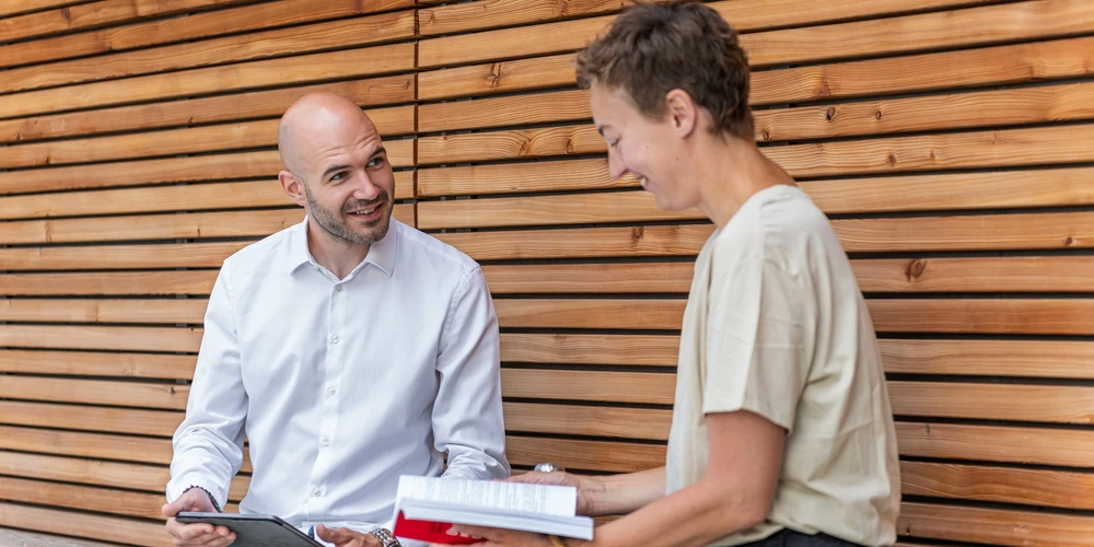 Berufsbegleitende Hochschulzertifikate und Fachseminare Zwei Studierende sitzen mit Büchern auf einer Bank in einer Holznische.