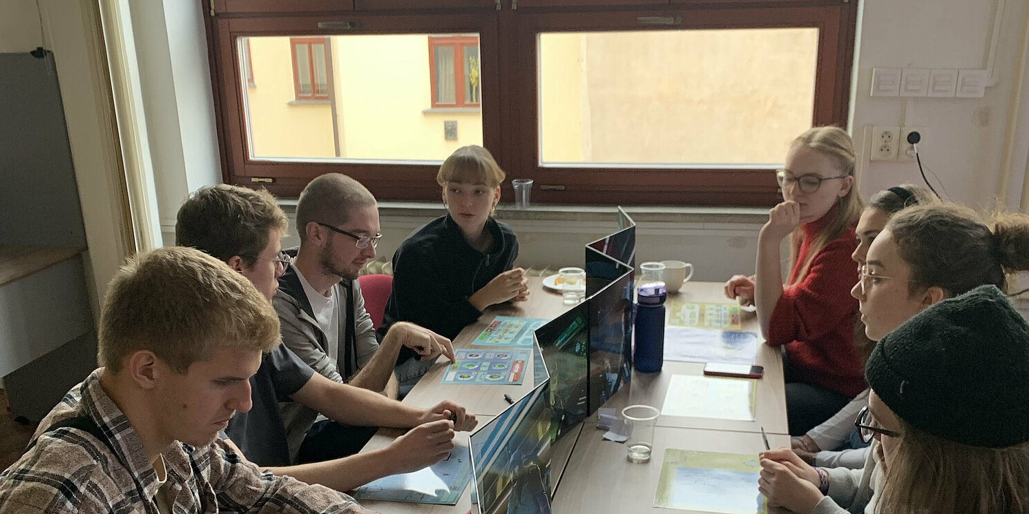 Teilnehmende sitzen um einen Tisch und spielen ein Spiel namens Captain Sonar.