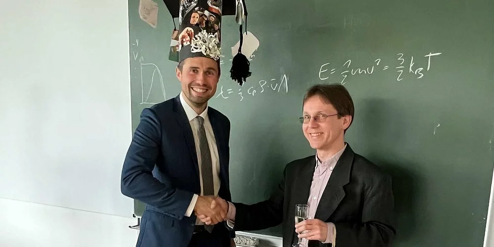 Prof. Dr. Rupert Schreiner (rechts) gratuliert dem Doktoranden Dominik Berndt, der mit einem originellen Doktorhut vor einer Tafel steht
