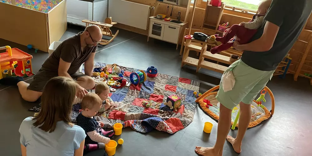 Eltern spielen mit ihren Kindern auf einer bunten Decke.