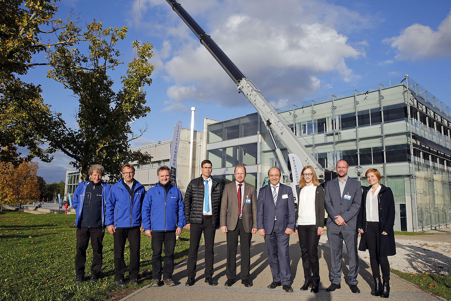 Die Verantwortlichen der Fakultät Maschinenbau der OTH Regensburg des achten Technik-Kolloquiums und die Vertreter von TADANO stehen vor dem riesigen Kran am Campus.