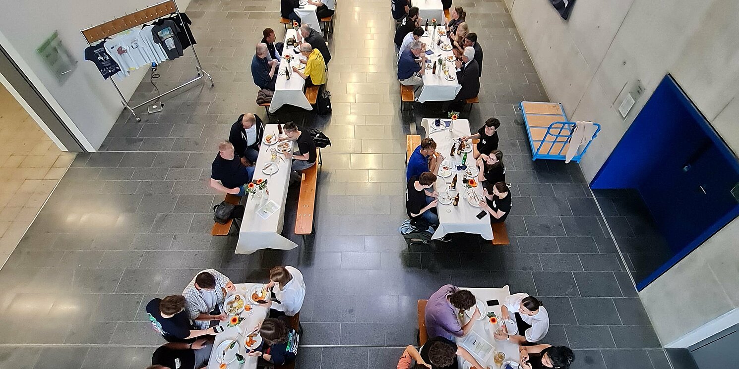 Blick von oben in ein Foyer, in dem Personen an Tischen sitzen.