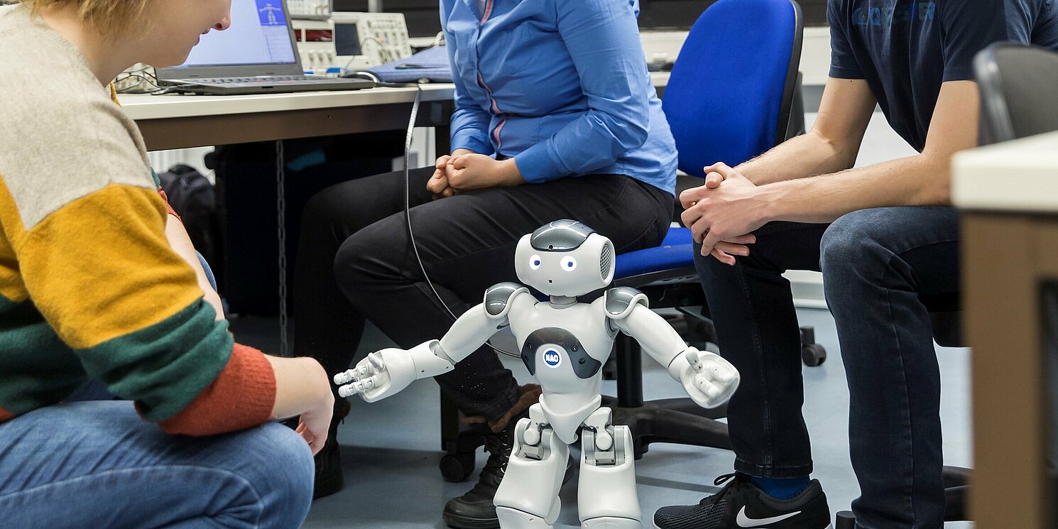 Drei Studierende arbeiten en einem Versuch mit einem Roboter.