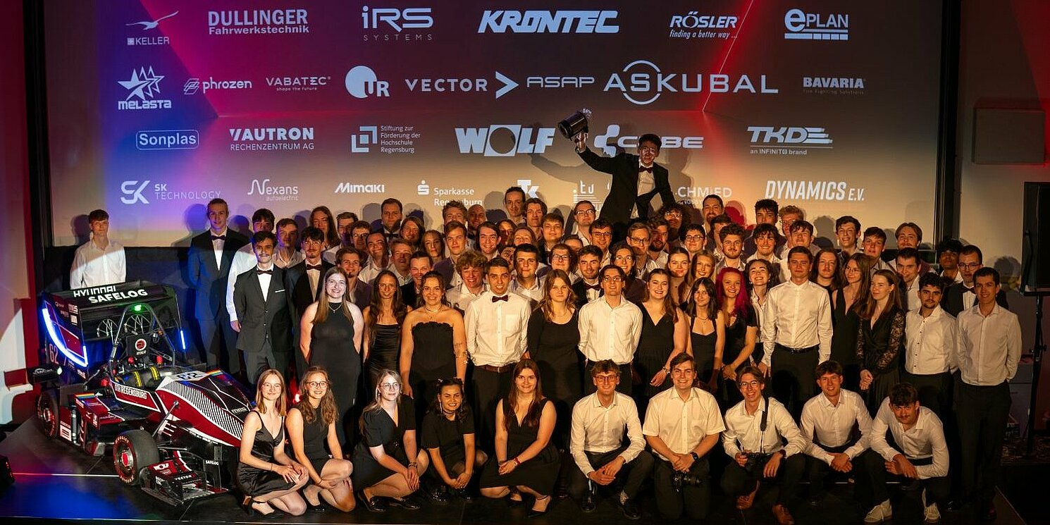 Gruppenfoto mit allen Teammitglieder von Dynamics e.V. auf der Bühne des Hörsaal S 054 der OTH Regensburg zusammen mit dem neuen Rennwagen RP 26 e/d