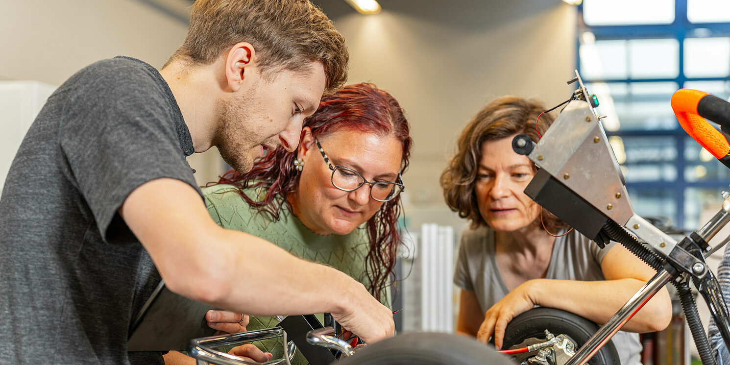 Automotive Electronics berufsbegleitend studieren Drei Studierende arbeiten an einem Fahrzeug.