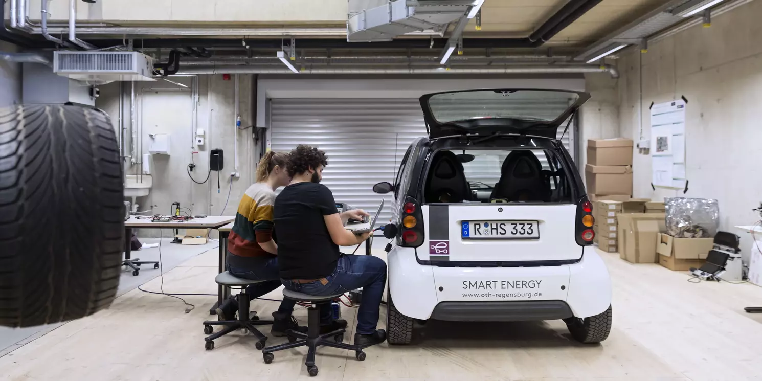 Zwei Studierende besprechen Messungen an einem E-Auto. 