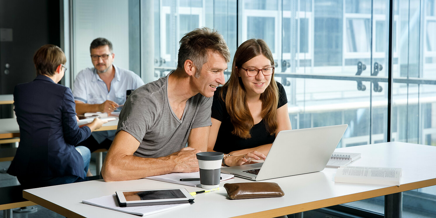 Vier Studierende lernen und arbeiten an ihren Tischen mit Büchern und Laptops