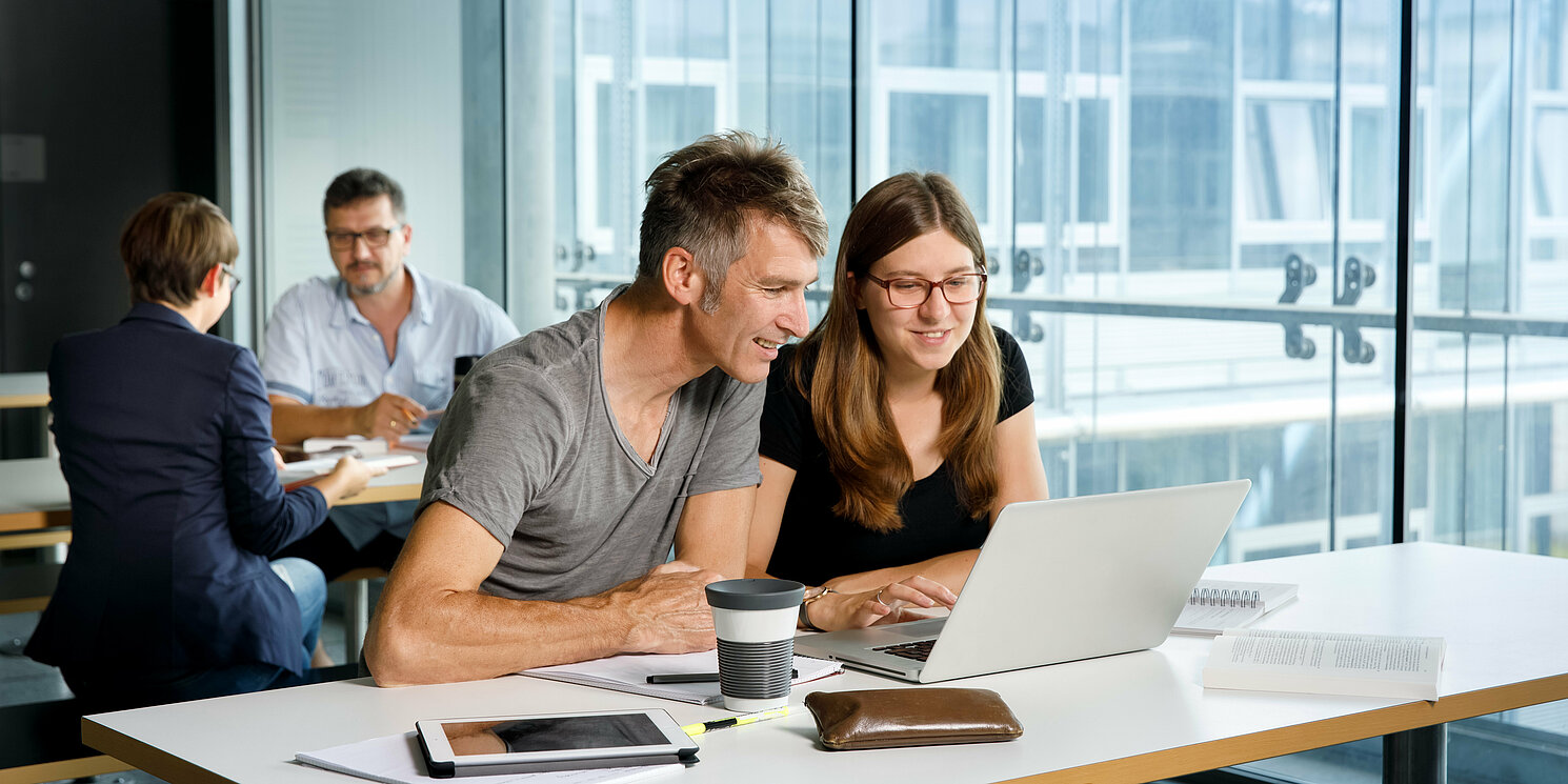 Business Administration berufsbegleitend studieren Vier Studierende lernen und arbeiten an ihren Tischen mit Büchern und Laptops