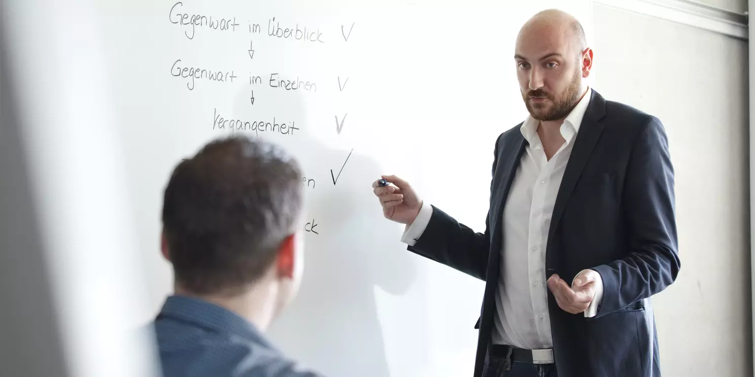 Modul Personalführung, Personalsteuerung und Personalentwicklung berufsbegleitend absolvieren Dozent steh an einem Whiteboard und erklärt einem Studenten etwas