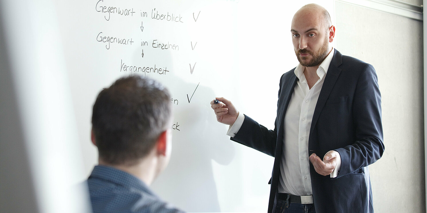 Dozent steh an einem Whiteboard und erklärt einem Studenten etwas