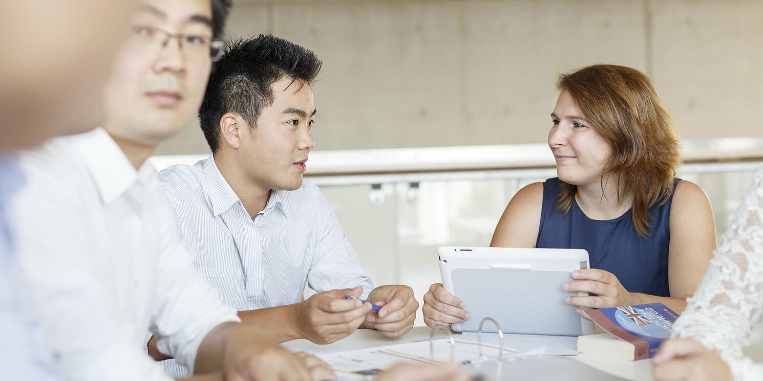 Fünf Studierende lernen und arbeiten an einem Tisch mit Büchern und Laptops 