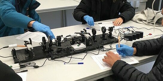 Drei Personen mit blauen Handschuhen bedienen technische Geräte.