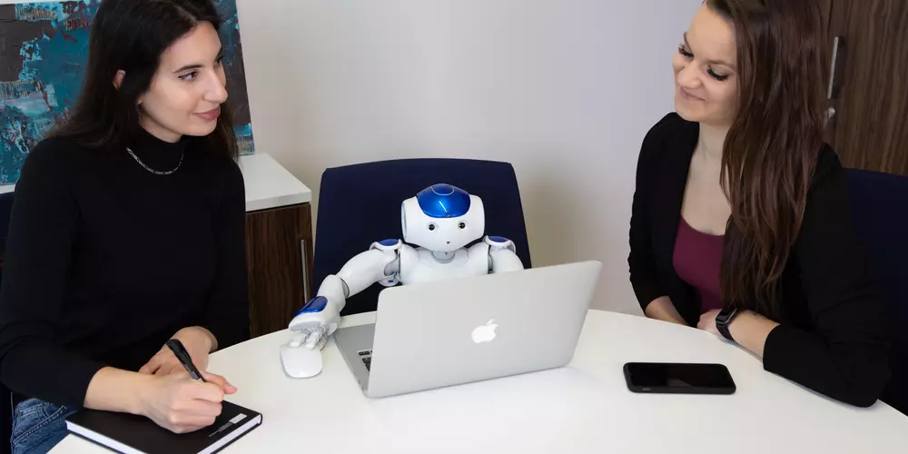Zwei Personen sitzen mit einem kleinen Roboter an einem Tisch