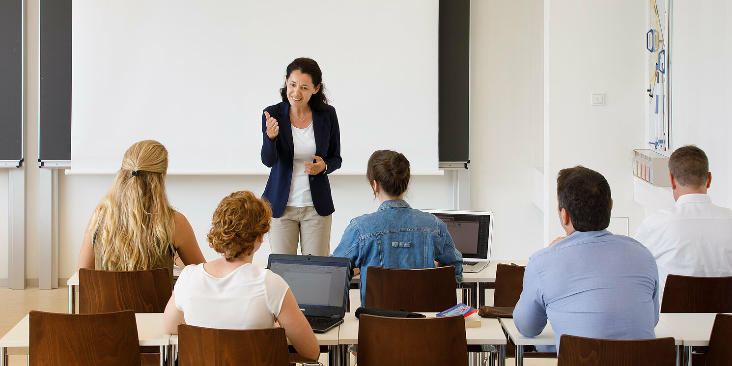 Dozentin mit fünf Studierenden in einem Seminarraum