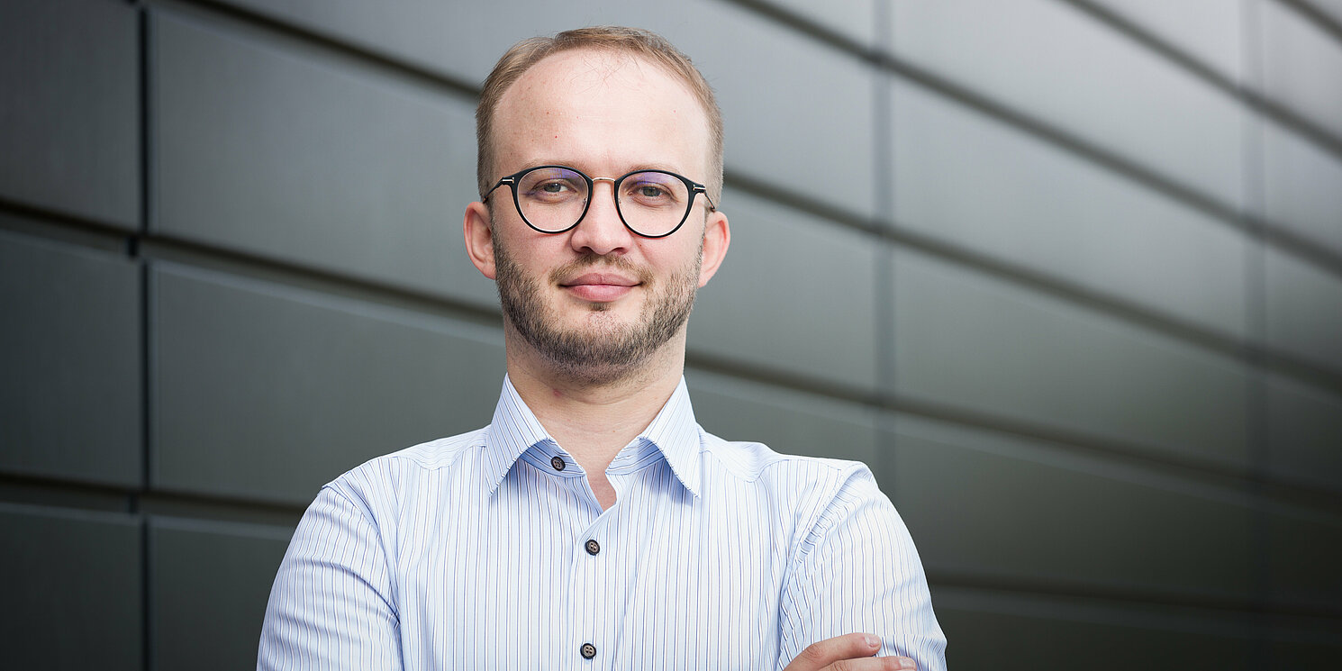 Ein Mann steht mit verschränkten Armen da und schaut in die Kamera.