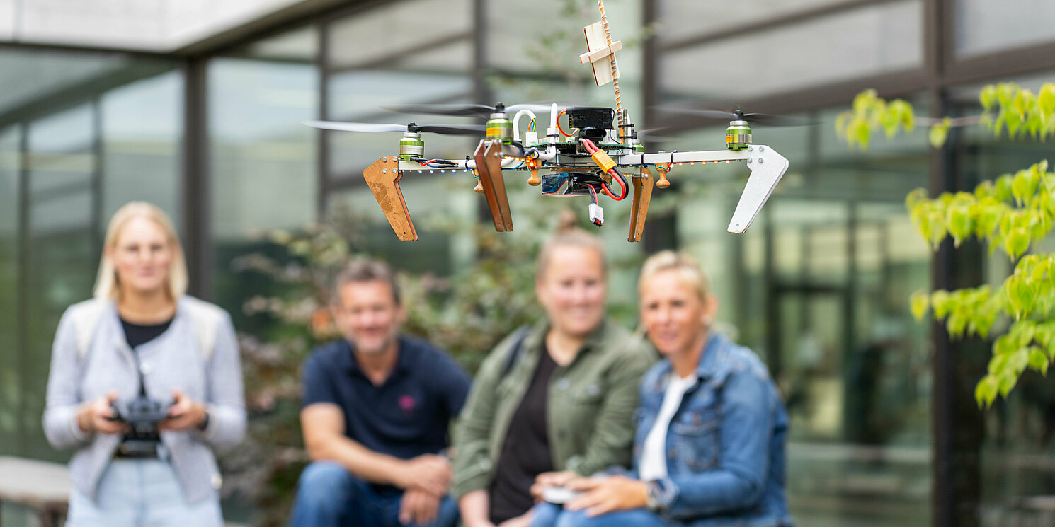 Studierende stehen in einem Innenhof und eine Studentin steuert eine fliegende Drohne.