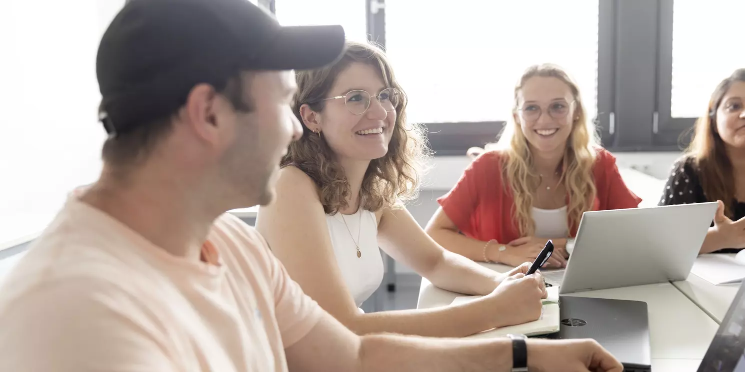 Vier Personen sitzen um einen Tisch. Auf dem Tisch sind Notebooks und Arbeitsunterlagen.