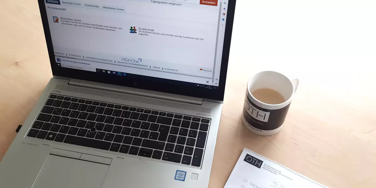 The photo shows a table with a computer and a cup of coffee. Notes are being taken on a block in preparation of the application.