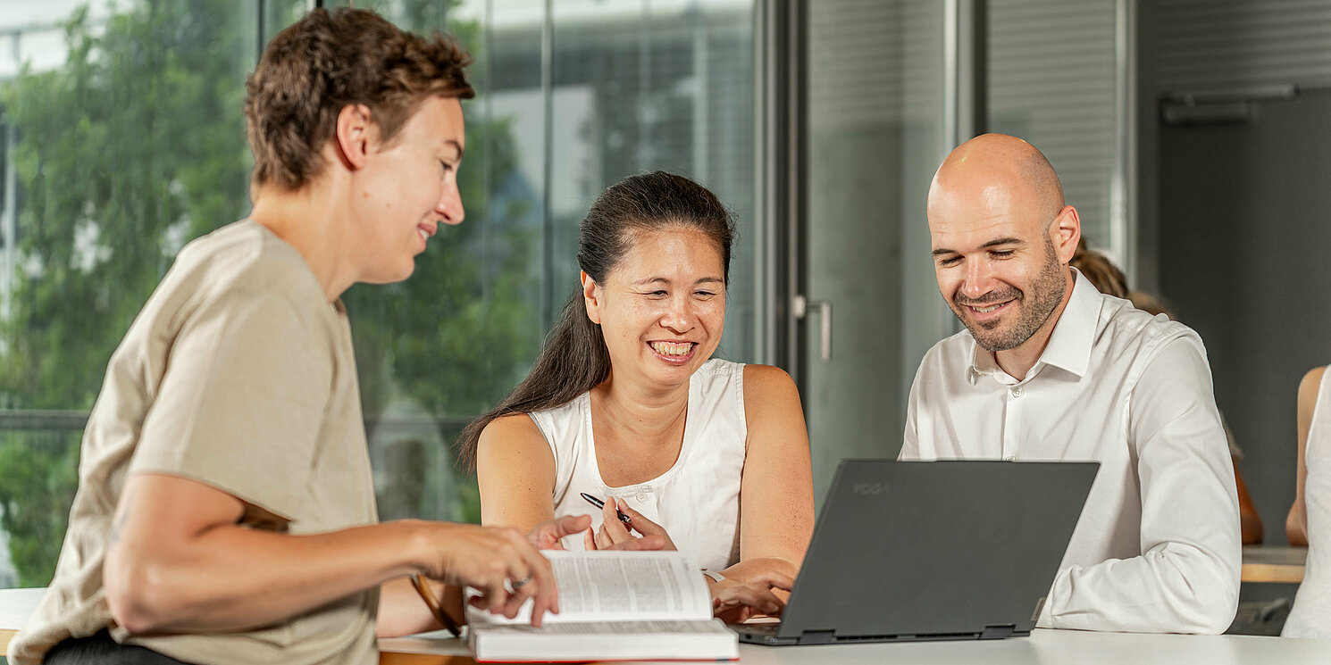 International Summer School: Trustworthy AI – Machine Learning Meets Blockchain Studiereden lernen an Tischen mit ihren Arbeitsmaterialien und unterhalten sich.