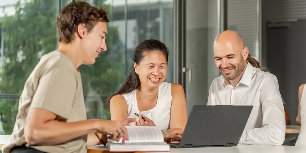 Studiereden lernen an Tischen mit ihren Arbeitsmaterialien und unterhalten sich.