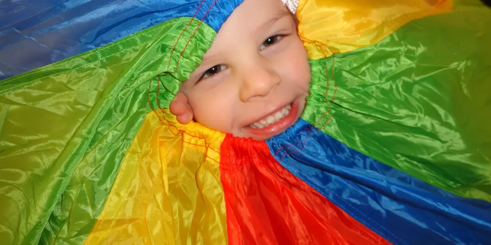 Ein lachendes Kindergesicht umrahmt von einem bunten Fallschirm