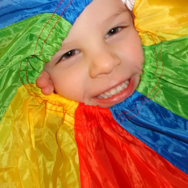 Ein lachendes Kindergesicht umrahmt von einem bunten Fallschirm