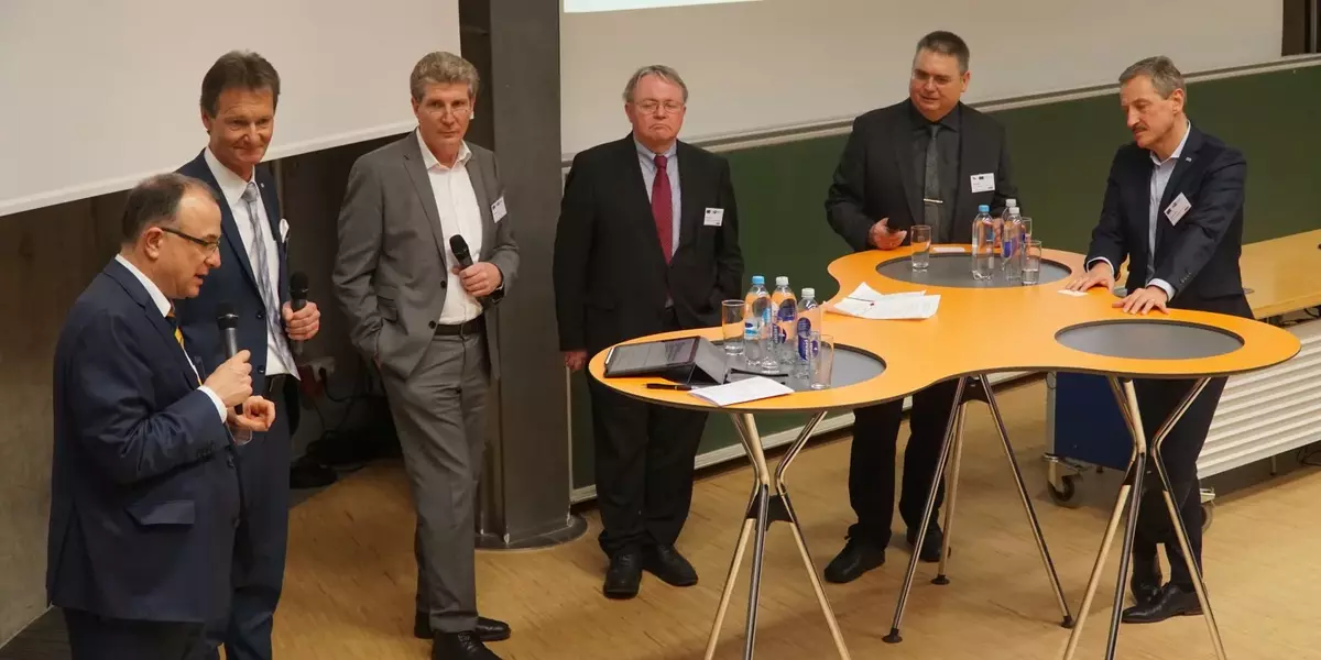 Podiumsdiskussion mit 6 stehenden Personen vor Stehtischen