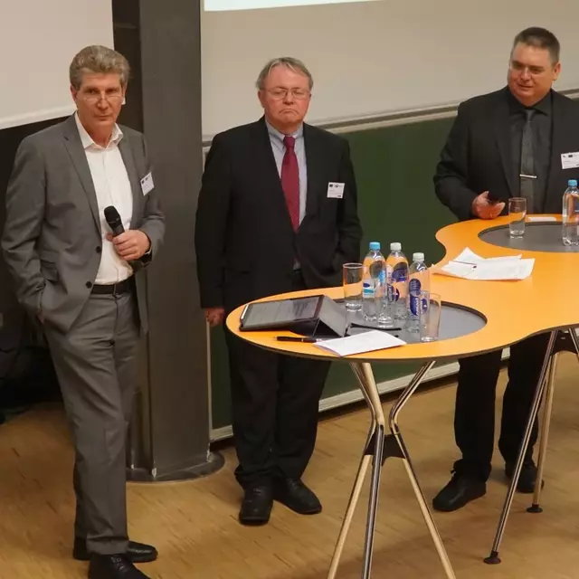 Podiumsdiskussion mit 6 stehenden Personen vor Stehtischen