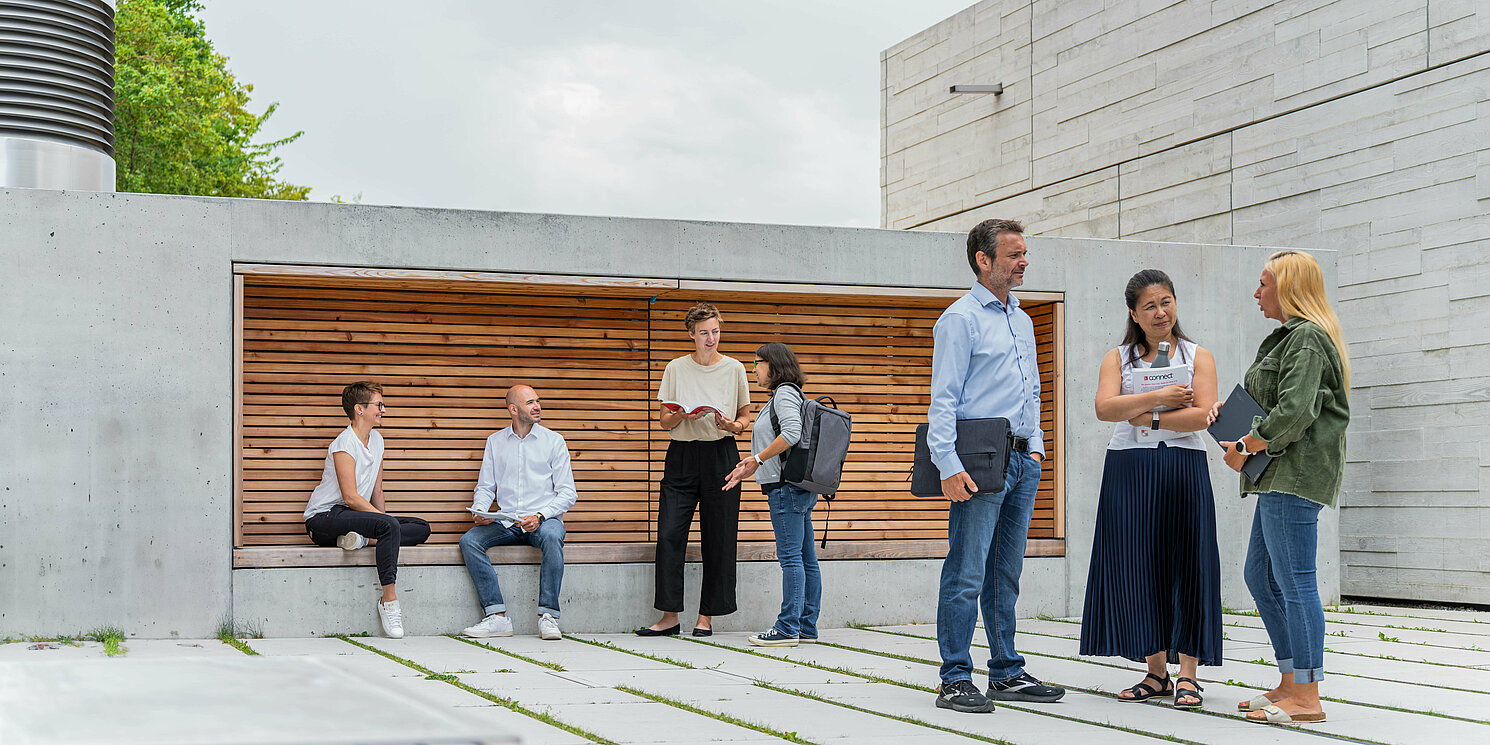 Studierende unterhalten sich vor einem Seminargebäude in mehreren Gruppen. 