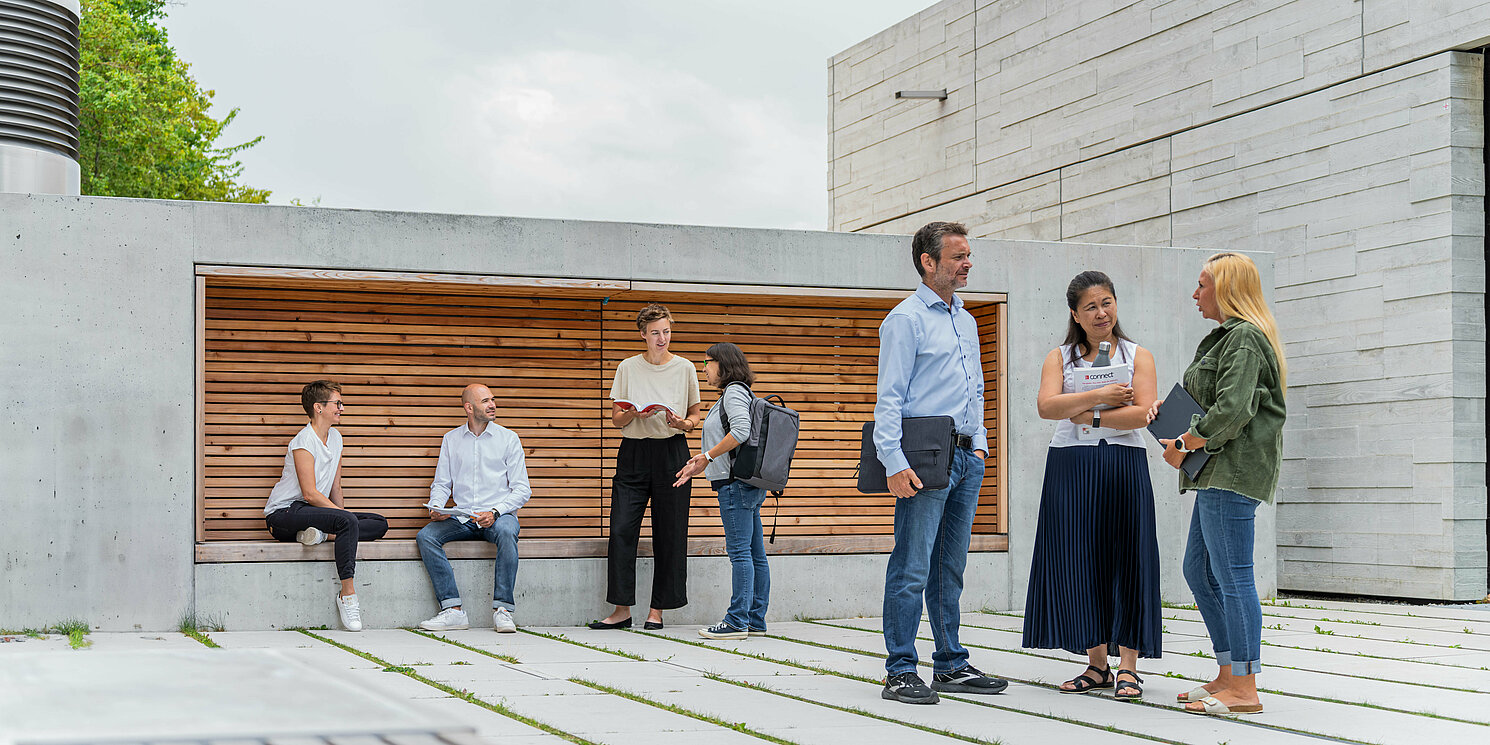 Studierende unterhalten sich vor einem Seminargebäude in mehreren Gruppen. 