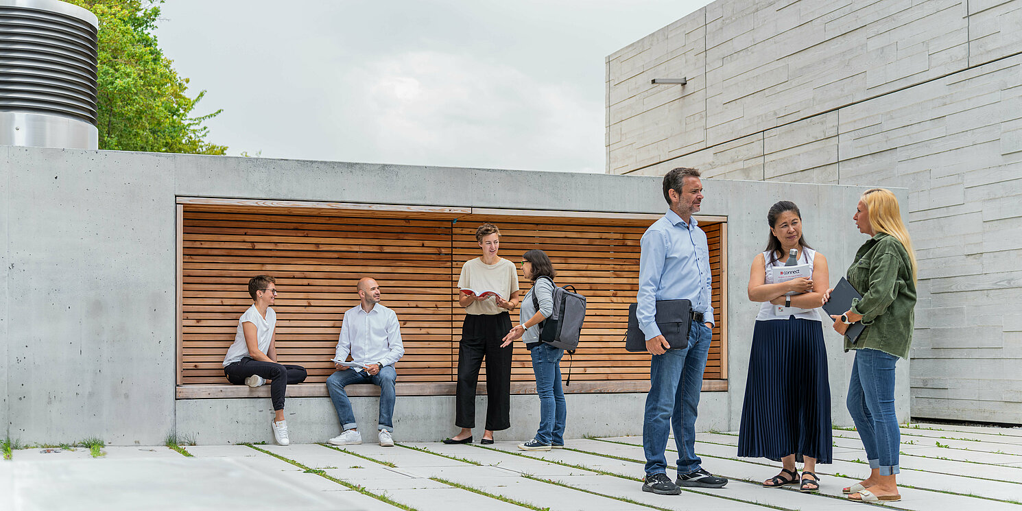 Studierende unterhalten sich vor einem Seminargebäude in mehreren Gruppen. 